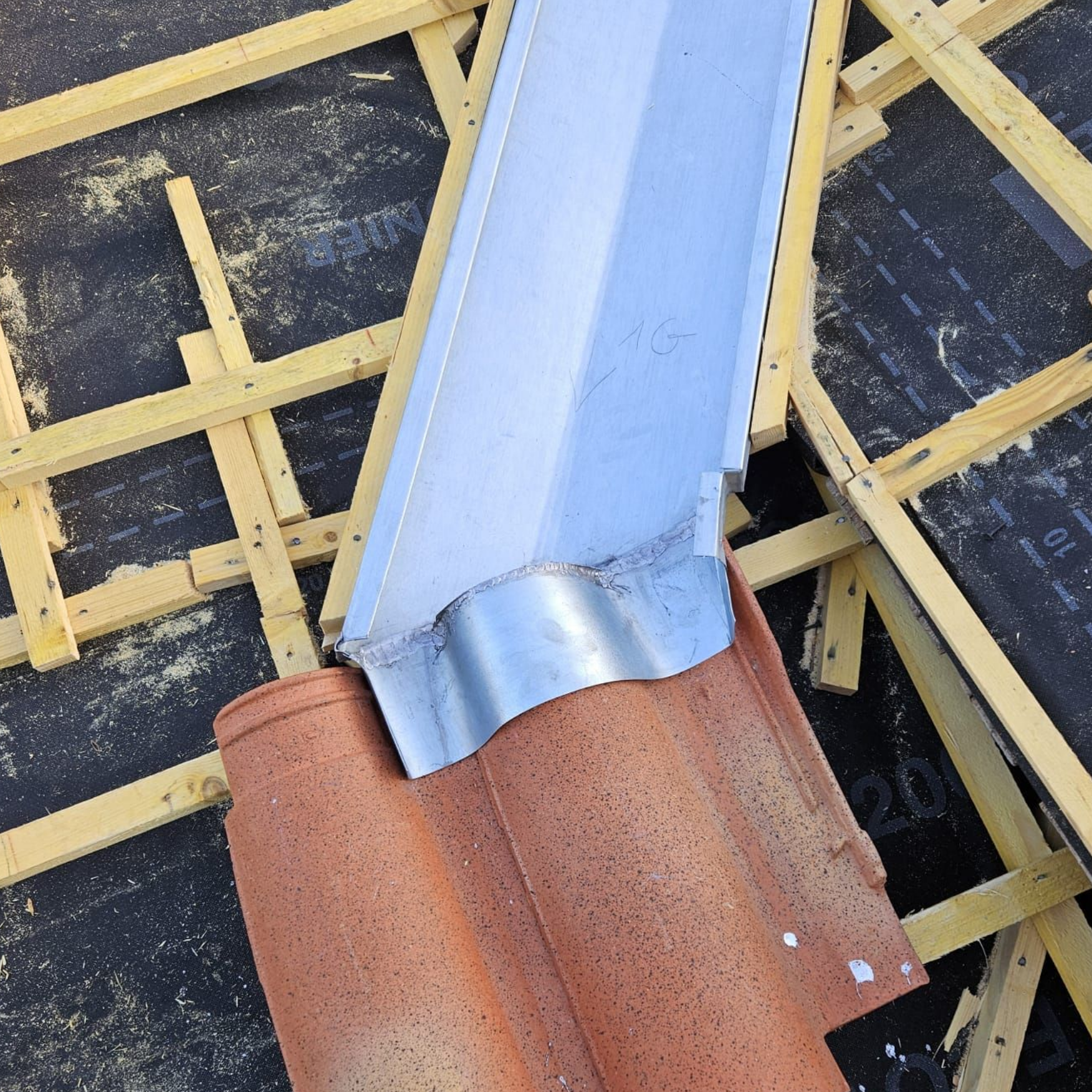 Toiture en construction avec poutres en bois apparentes et une gouttière et un tuyau de descente nouvellement installés.