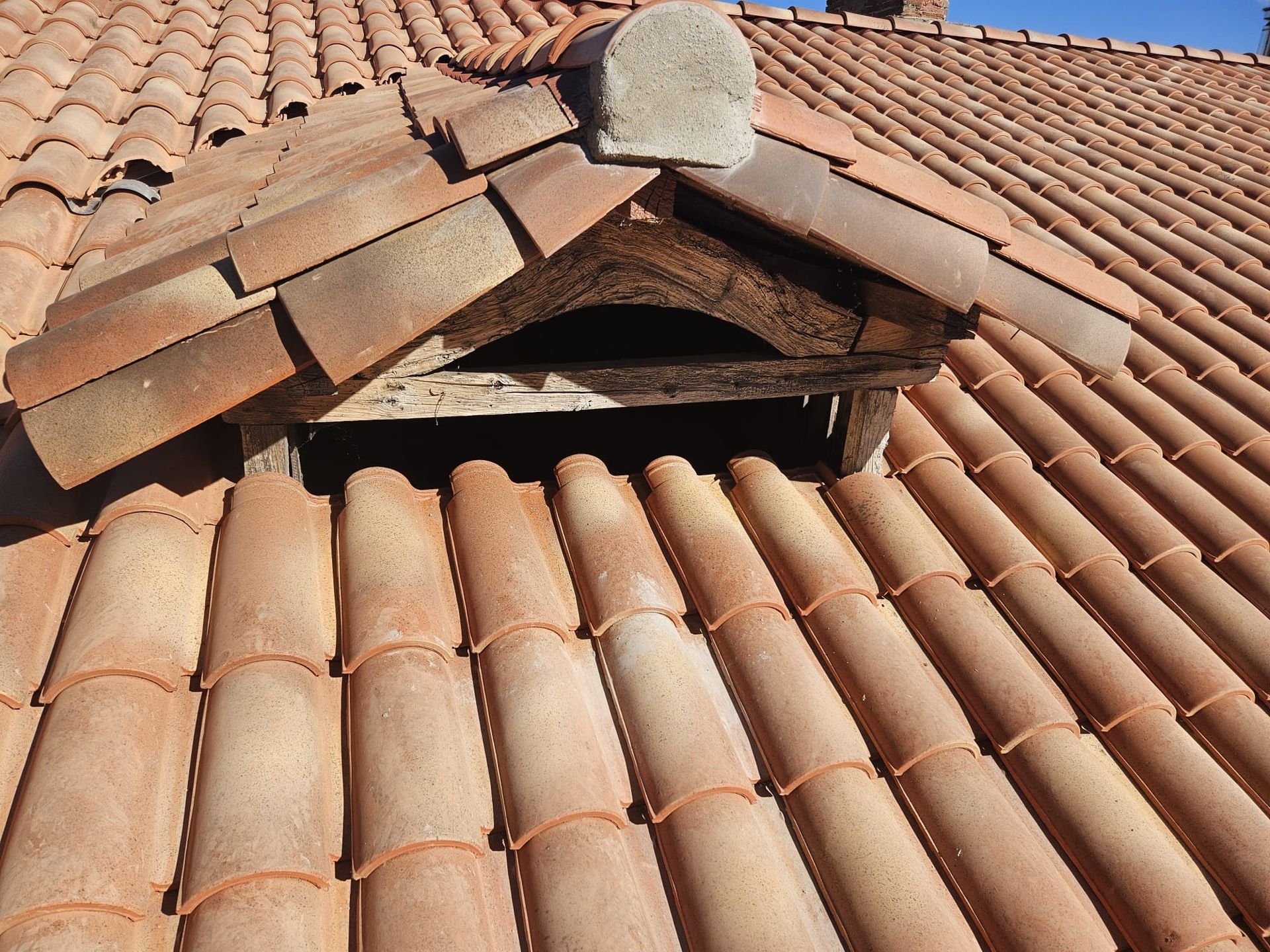 Toiture en tuiles d'argile avec une ventilation ouverte, une ossature en bois apparente et un petit capuchon en pierre.