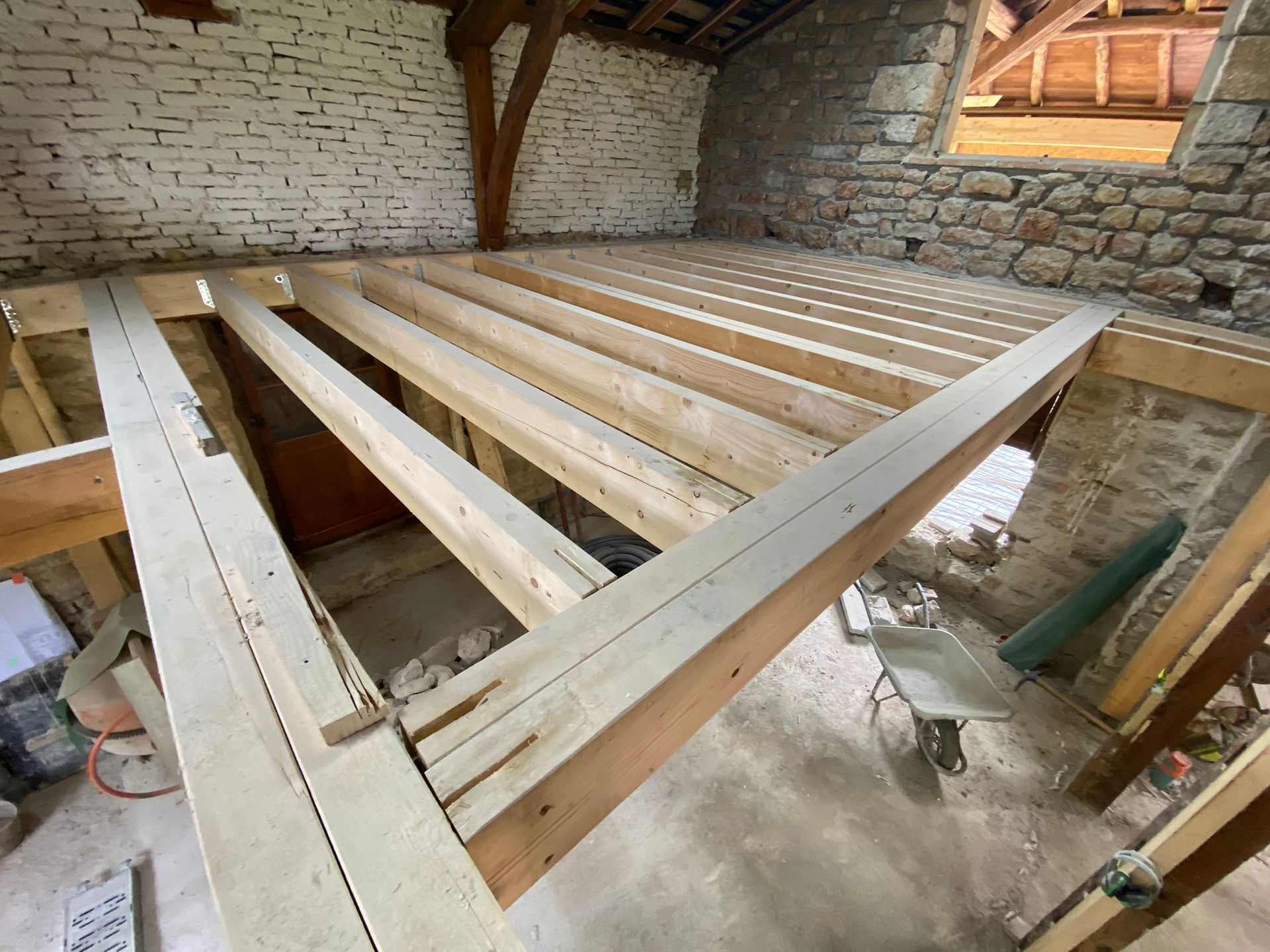 Construction d'une ossature de plancher en bois dans une pièce avec des murs en pierre et en brique.