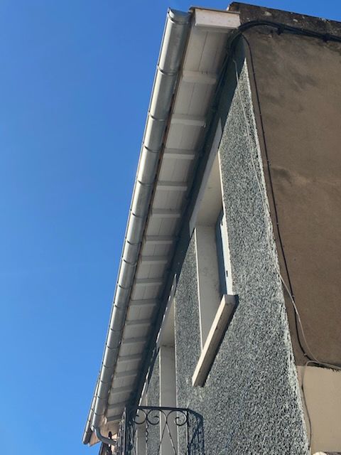 Vue latérale d'un bâtiment avec une gouttière blanche, une fenêtre et un balcon contre un ciel bleu.