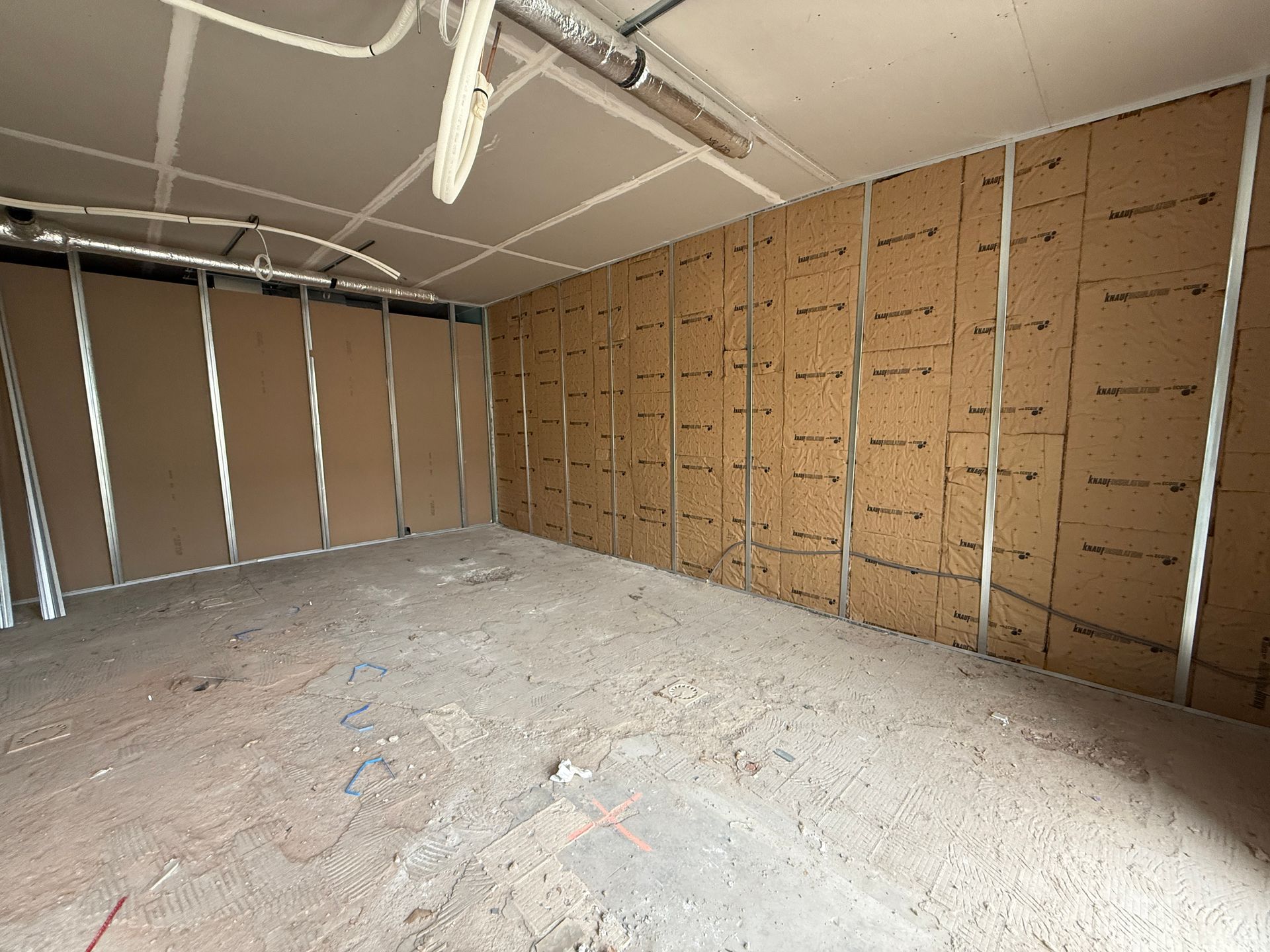 Chambre en construction, charpente métallique et isolation sur les murs, plancher de béton apparent, plafond brut.