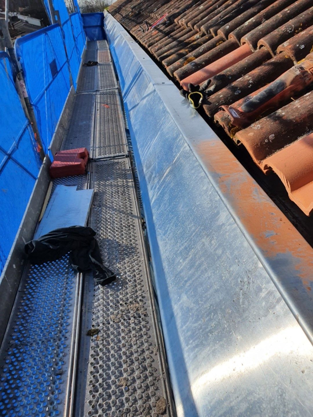 Gouttière métallique le long d'un toit en tuiles, avec échafaudage visible à gauche.