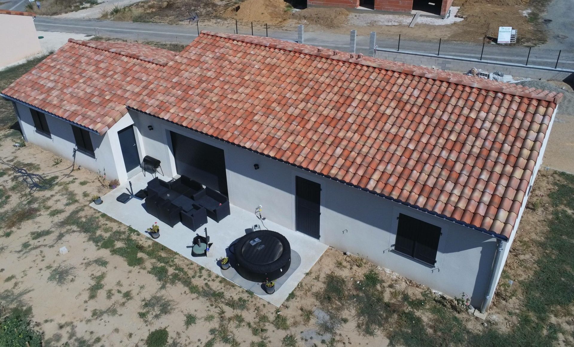 Vue aérienne d'une maison à un étage avec un toit en tuiles en terre cuite et un patio en béton.