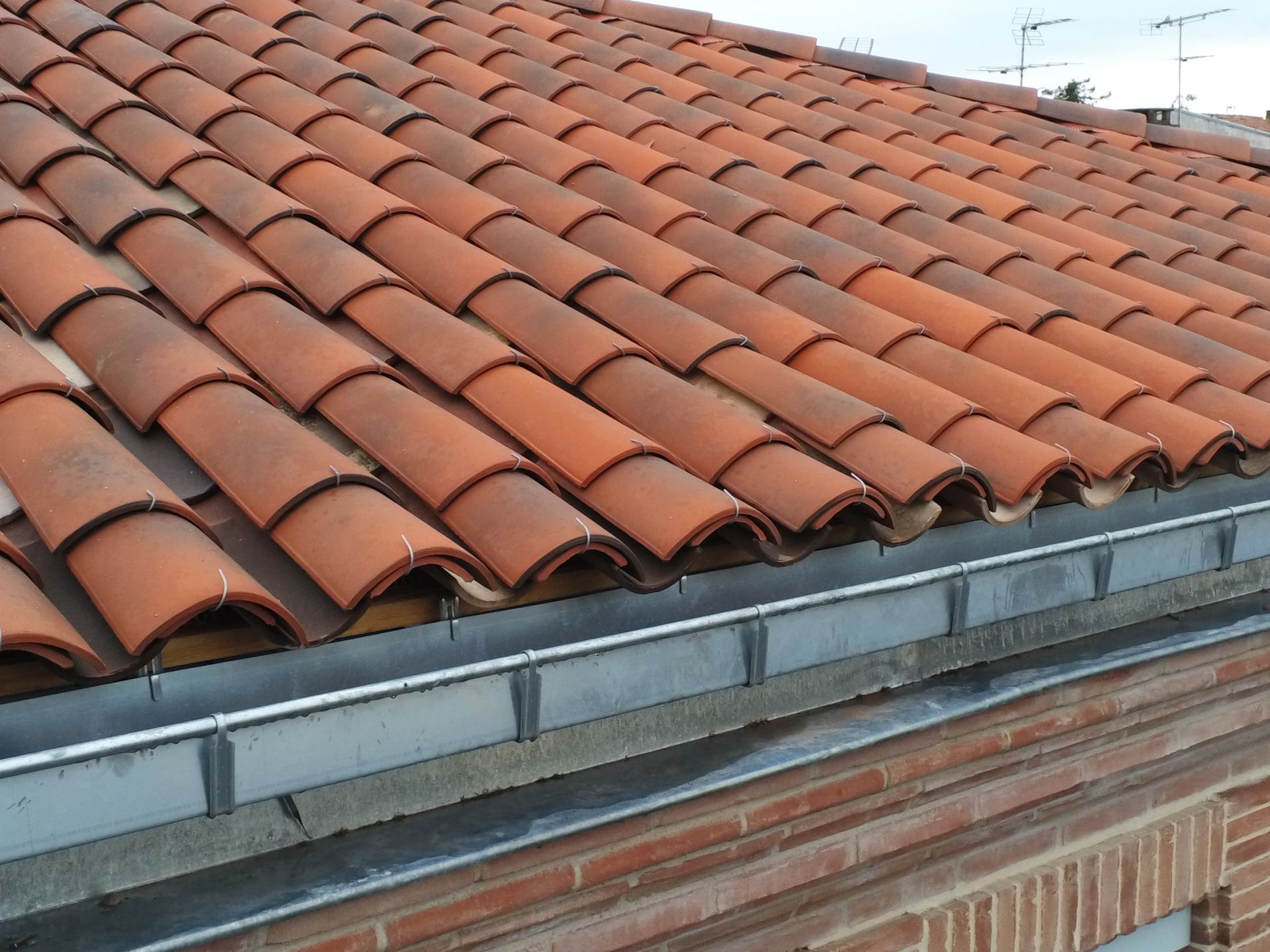 Toiture en tuiles rouges avec gouttière métallique et mur en briques.