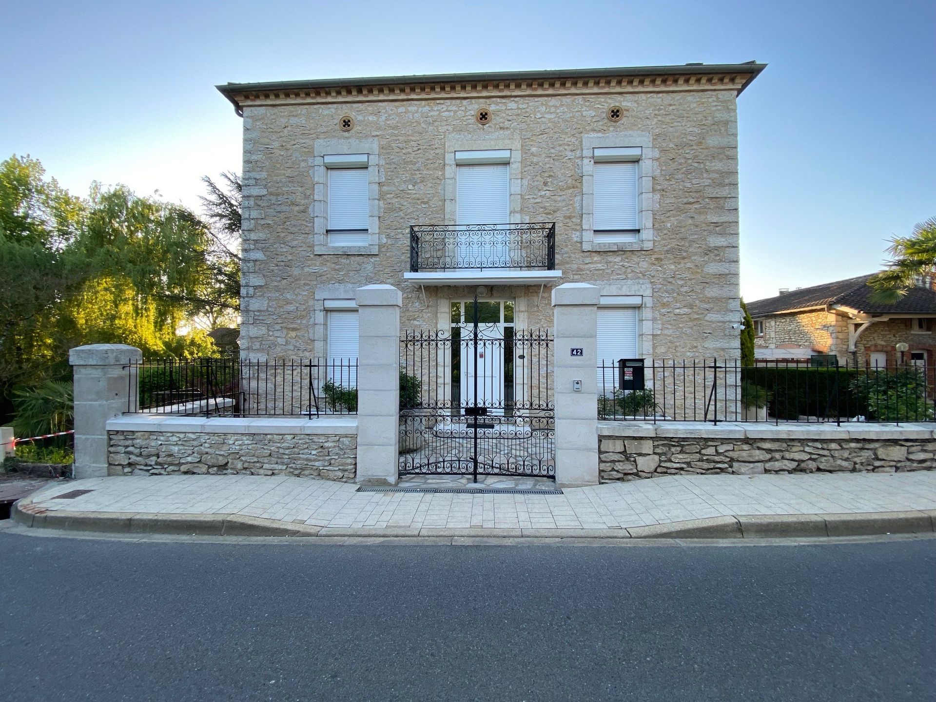 Maison en pierre à deux étages avec portail en fer noir et balcon.