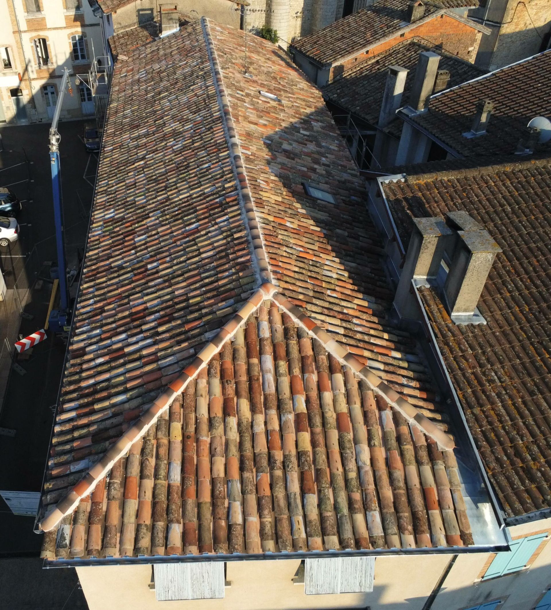 Vue aérienne d'un bâtiment avec un long toit en tuiles ; tuiles en terre cuite de différentes couleurs ; lumière du soleil.