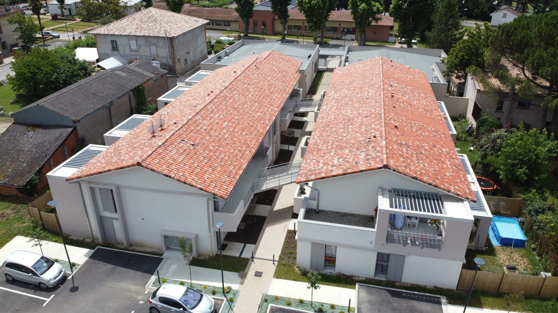 Bâtiments aux toits de tuiles rouges et aux murs blancs, voitures garées devant.