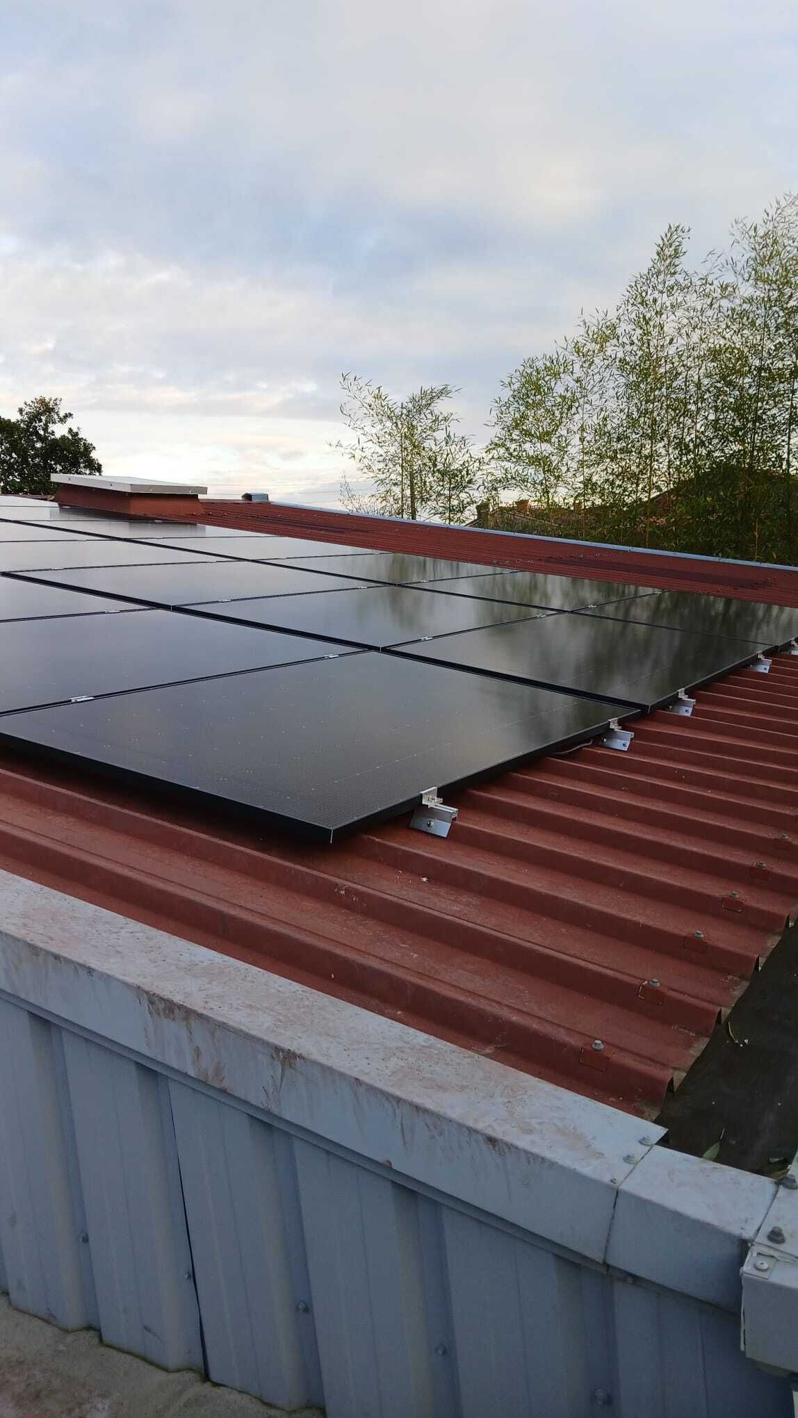 Panneaux solaires sur un toit en tôle ondulée rouge, ciel nuageux en arrière-plan.