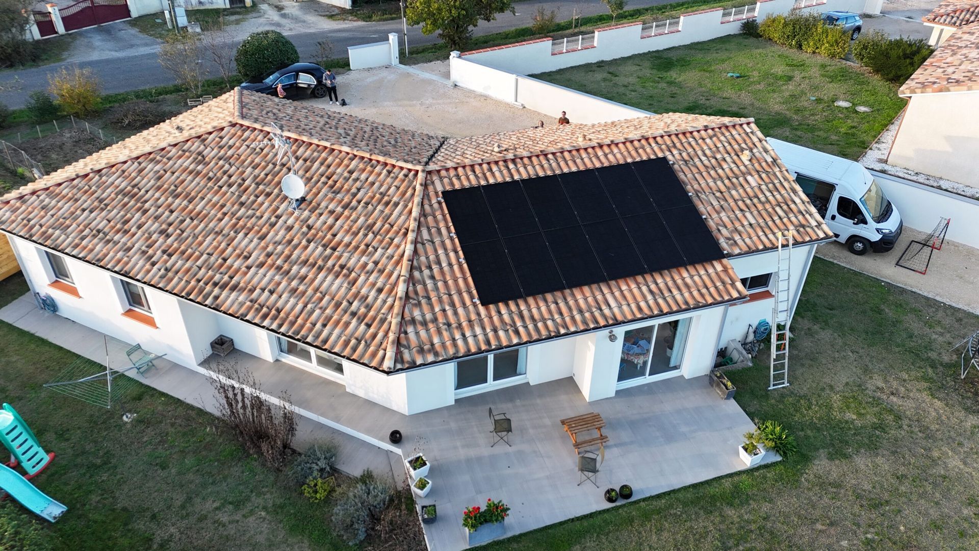 Vue aérienne d'une maison avec des panneaux solaires sur le toit, un patio et une camionnette garée à proximité.