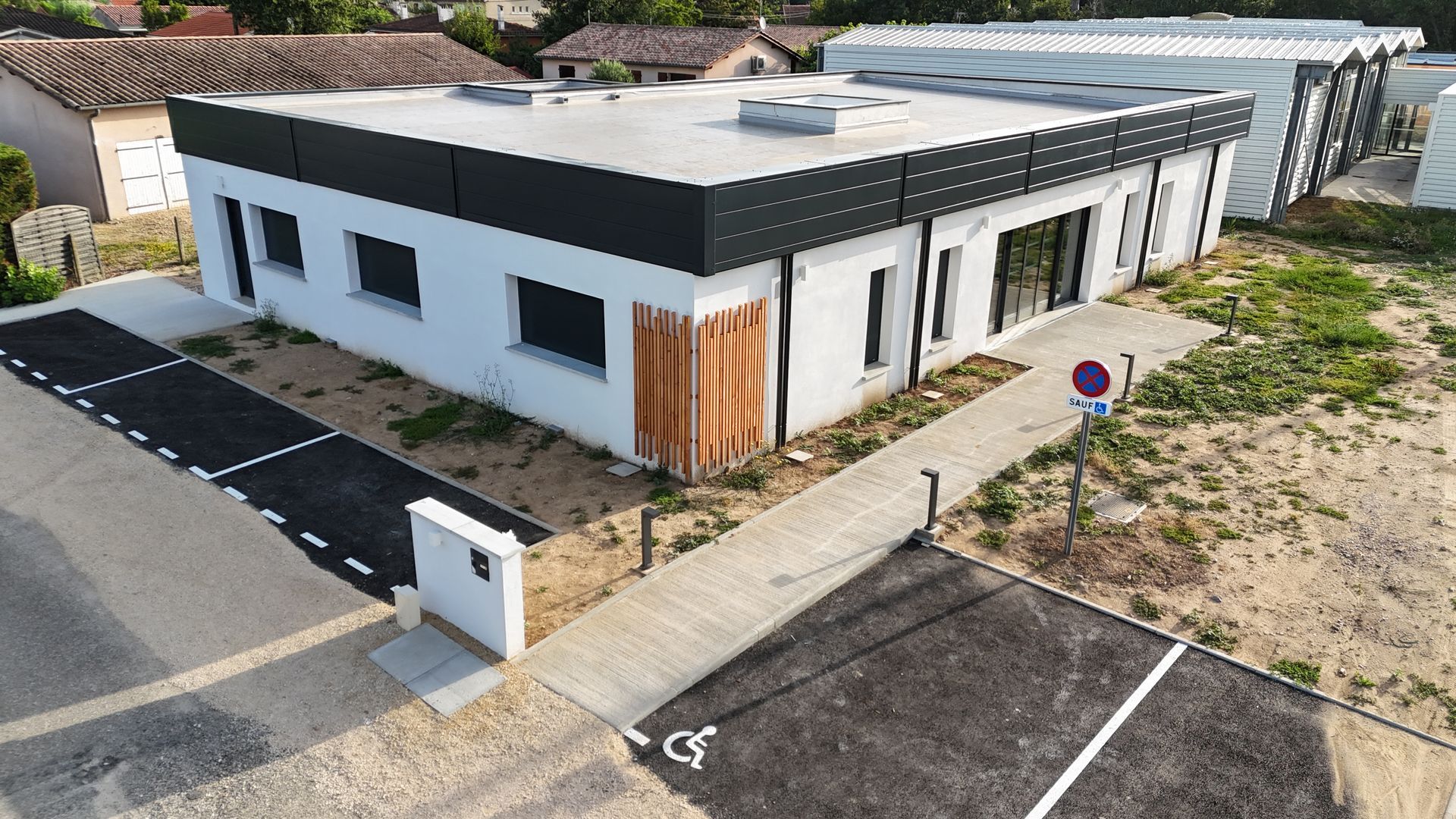 Un bâtiment blanc d'un étage avec un toit plat, des garnitures noires et une rampe d'accessibilité.