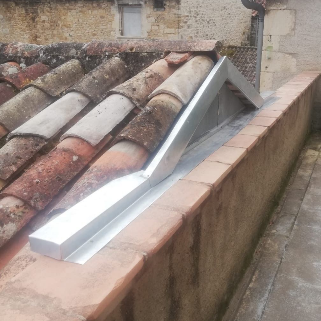 Système de gouttières noires le long du bord d'une maison beige clair avec un toit en tuiles rouges, contre un ciel bleu.