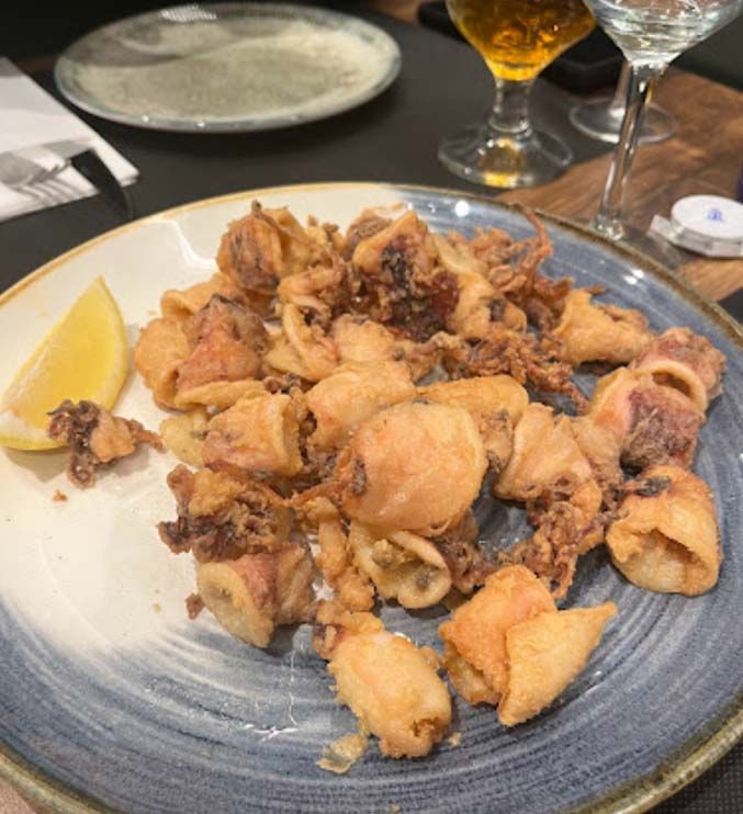 Un plato de calamares fritos con una rodaja de limón sobre una mesa.