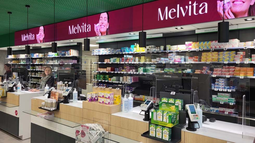 Intérieur d'un magasin avec caisses enregistreuses, étagères de produits et enseigne Melvita. On aperçoit des personnes derrière les comptoirs.