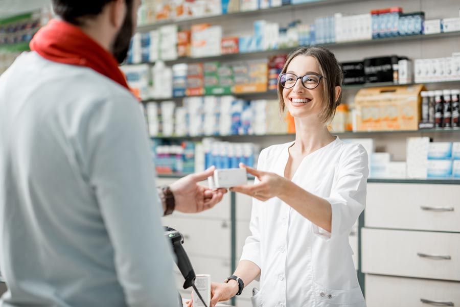Dans une pharmacie, un pharmacien remet une boîte de médicaments à un client, tous deux souriant.