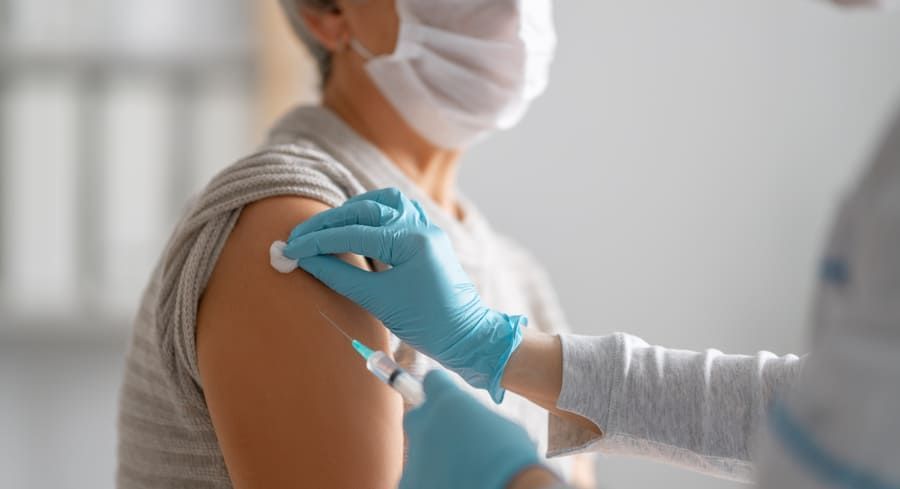 Personne recevant une vaccination au bras ; professionnel de santé administrant l’injection avec des gants bleus.
