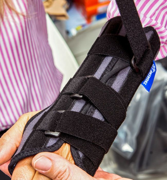 Main portant une attelle de poignet noire avec des sangles Velcro, tenue par une personne.