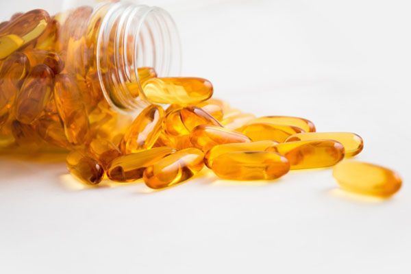 Des capsules jaunes et ovales se répandent d'un flacon transparent sur une surface blanche.