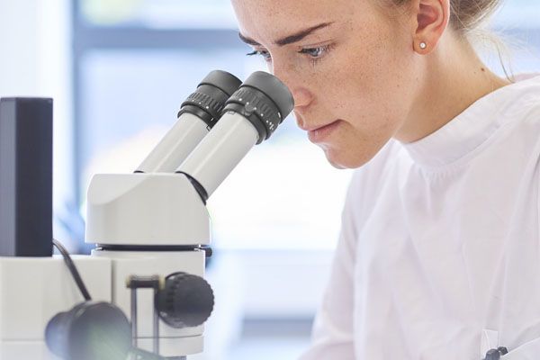 Une femme en blouse blanche observe au microscope dans un laboratoire.