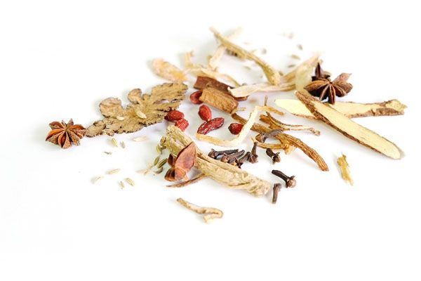 Assortiment d'herbes et d'épices séchées dispersées sur une surface blanche, dont de l'anis étoilé et des baies de goji.