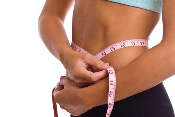 Une femme mesure son tour de taille avec un mètre ruban rose.