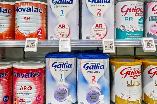 Des étagères remplies de boîtes de lait infantile de différentes marques comme Gallia, Novalac et Guigoz.