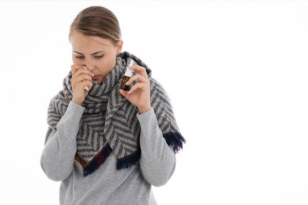 Femme utilisant un spray nasal, enveloppée dans une écharpe, regardant vers le bas.