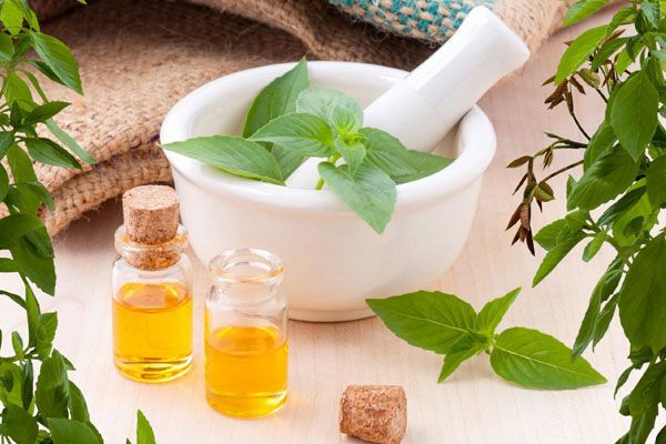 Mortier et pilon blancs ornés de feuilles, de petites bouteilles ambrées et de feuillage.