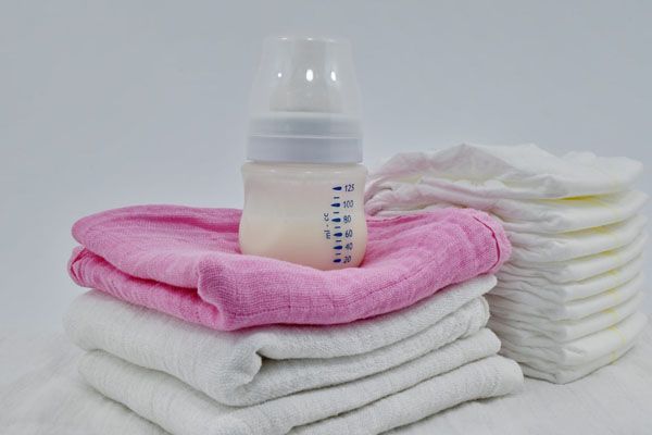 Biberon sur des langes roses et blancs, pile de couches en arrière-plan.