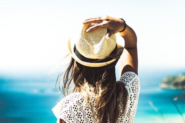 Une femme coiffée d'un chapeau de paille regarde l'océan.