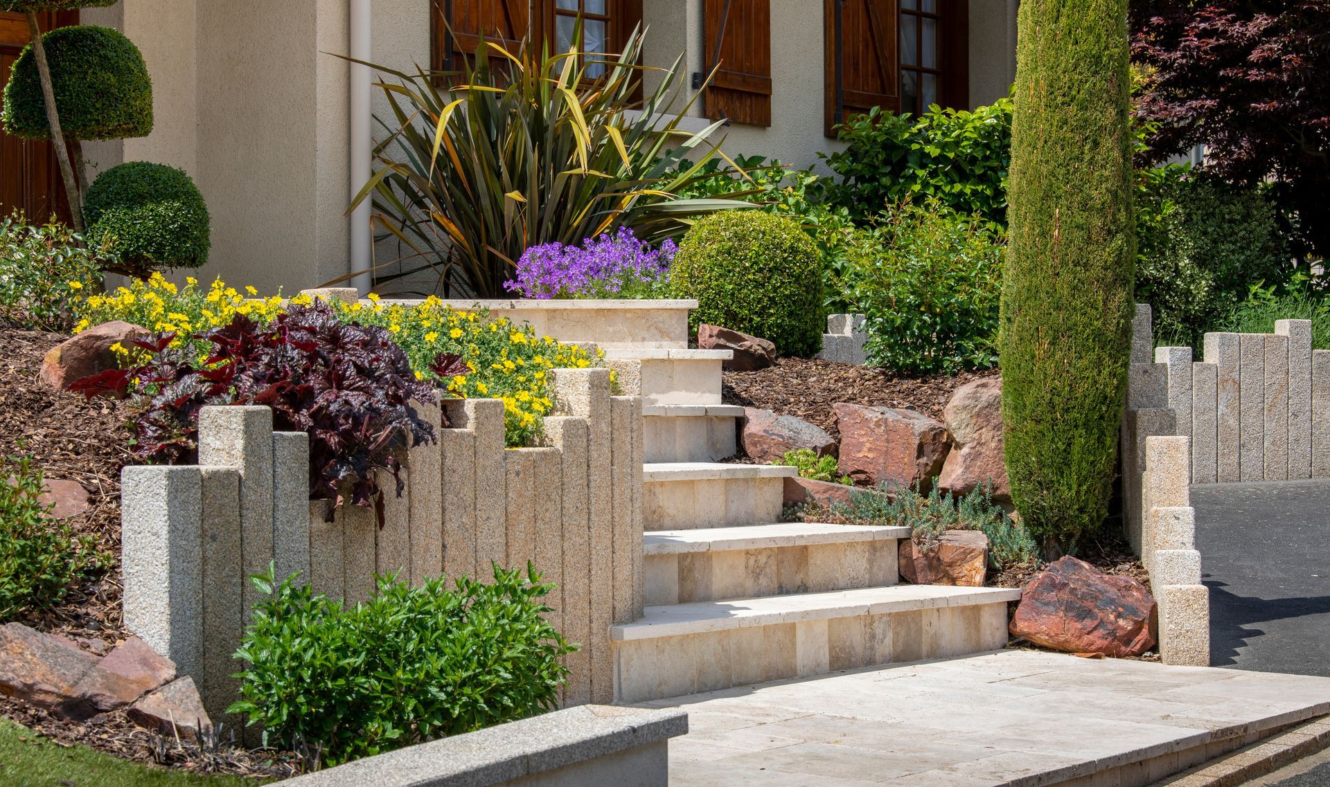 Escalier d'entrée et jardin paysager avec murs de soutènement en pierre, fleurs colorées et entrée de la maison.