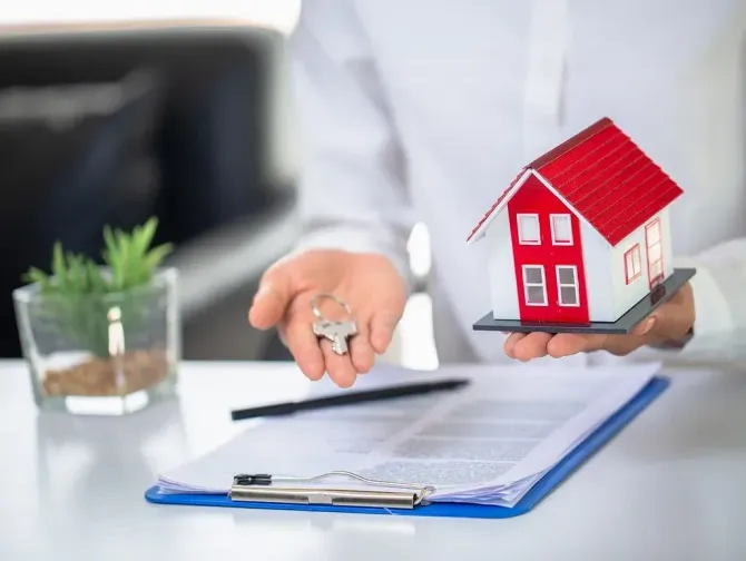 Persona con maqueta de casa, llaves y contrato; camisa blanca; compra de vivienda.