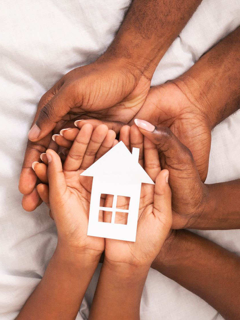 Des mains tenant une petite maison en papier rouge.