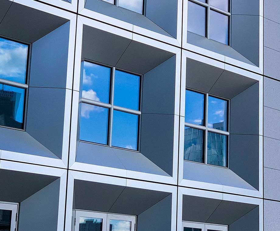 Façade d'immeuble moderne avec des fenêtres carrées en retrait reflétant un ciel d'un bleu éclatant.