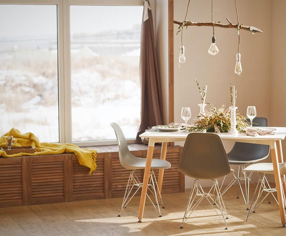 Salle à manger avec une table blanche, des chaises modernes, une fenêtre donnant sur un paysage enneigé et un luminaire en forme de branche.