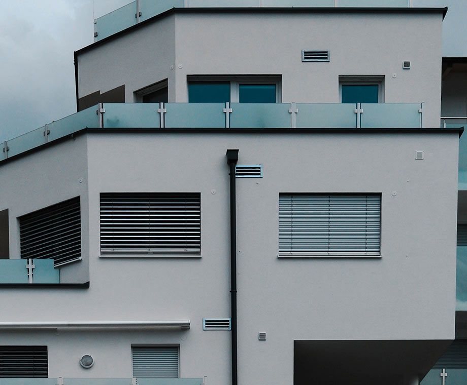 Bâtiment blanc moderne avec garde-corps en verre, fenêtres à stores et descente de gouttière sombre.