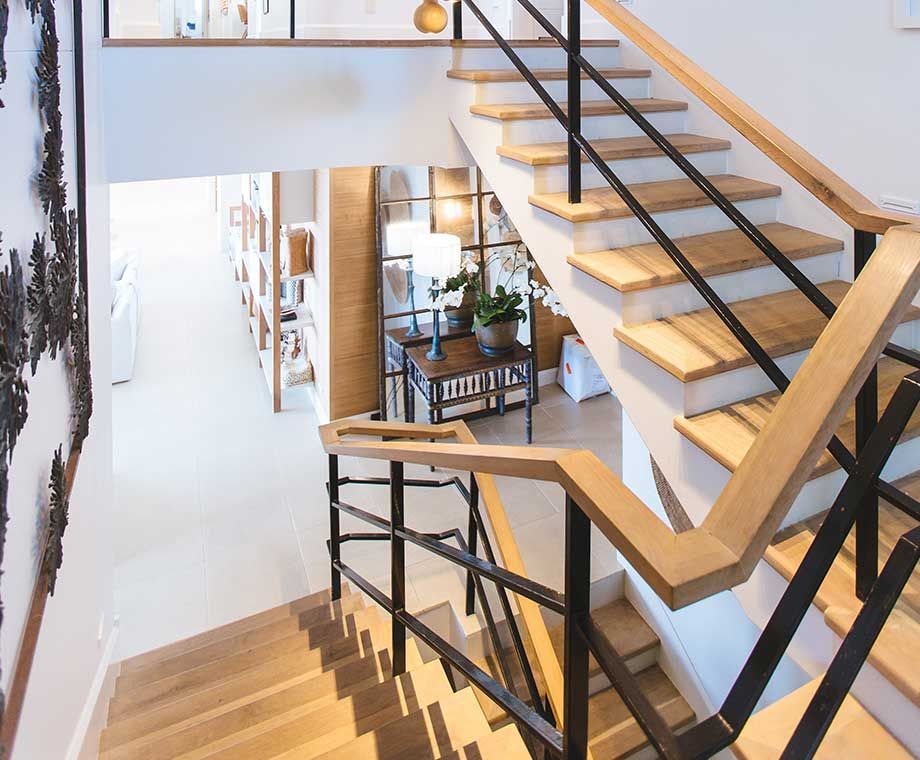 Un escalier en bois avec une rampe noire mène à une entrée lumineuse et ouverte.