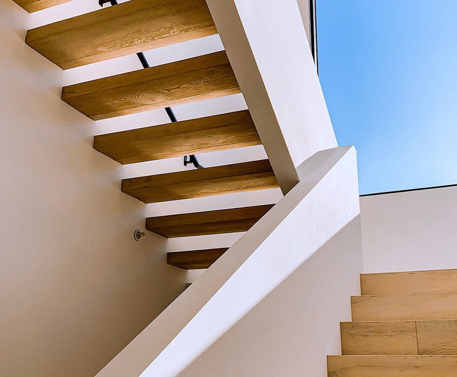 Escalier en bois avec supports en métal noir, murs blancs et ciel bleu visible.