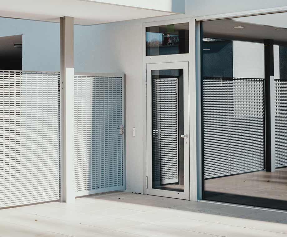 Extérieur d'un bâtiment moderne avec un portail et une porte en métal, reflétant la lumière.