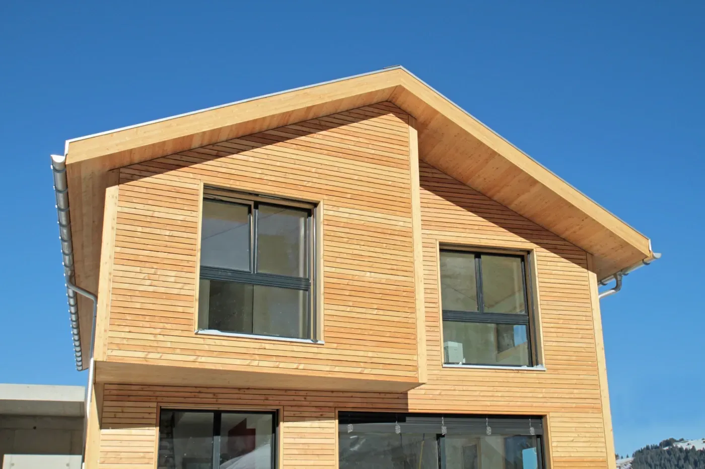 Modernes Holzhaus mit großen Fenstern und schrägem Dach unter klarem, blauem Himmel