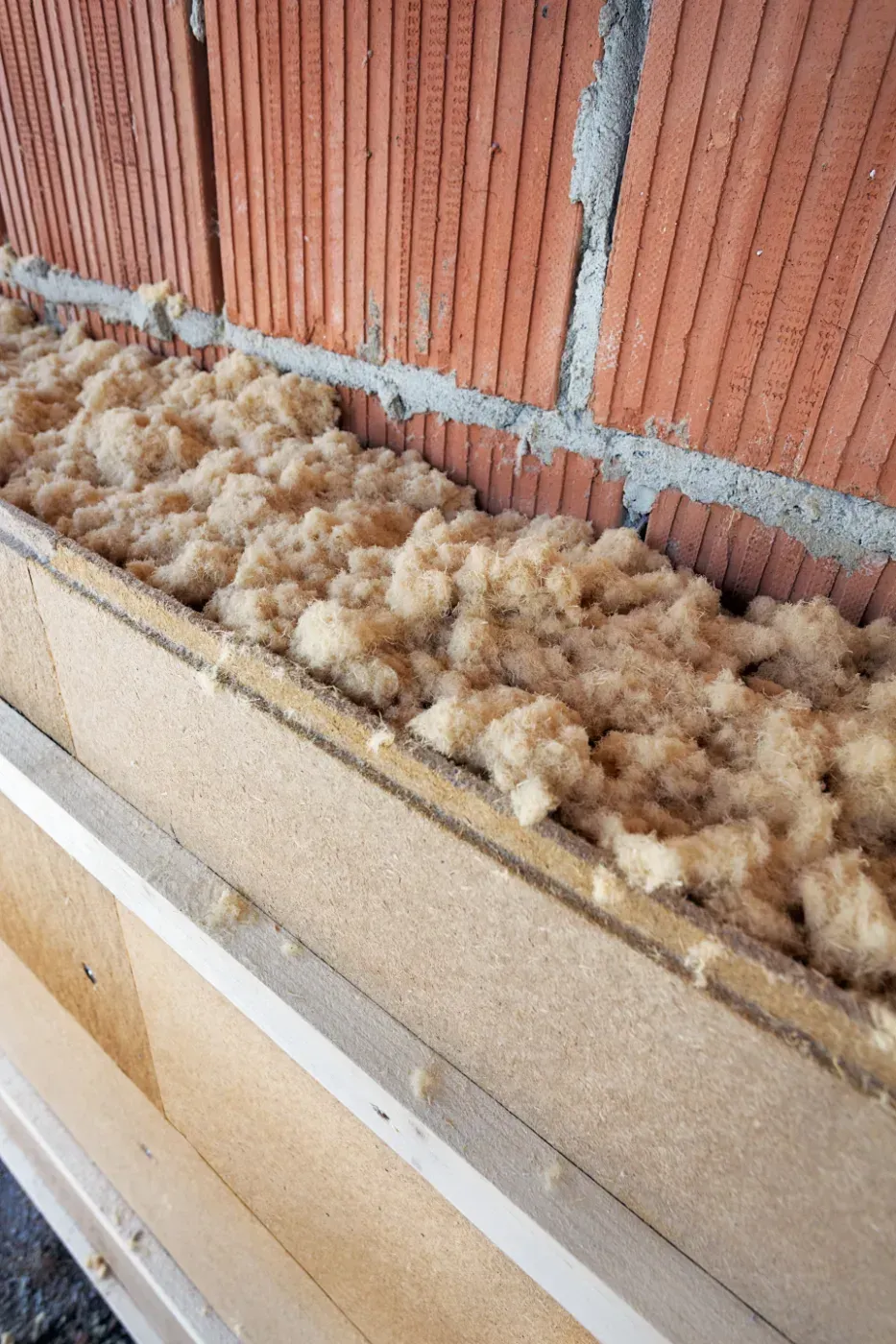 Dämmmatten oberhalb einer Ziegelwand und Sperrholzverkleidung in einer unfertigen Innenwand