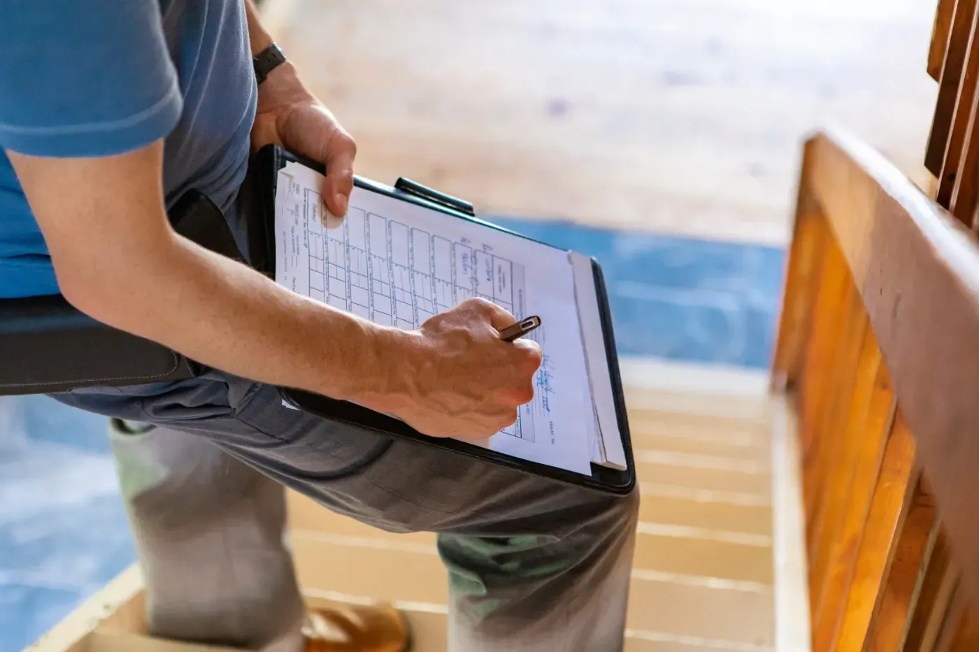 Person füllt im Sitzen auf einer Treppe in einem Innenraum eine Checkliste auf einem Klemmbrett aus.