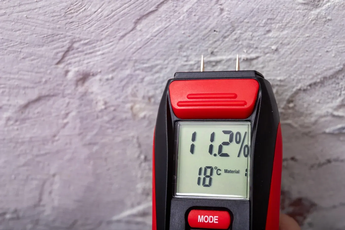 Ein digitales Thermometer zeigt 11,2 % Luftfeuchtigkeit und 18 °C an einer strukturierten Wand an.