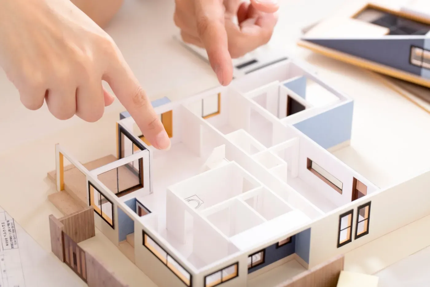 Hände zeigen auf ein Miniatur-Hausgrundrissmodell auf einem Schreibtisch