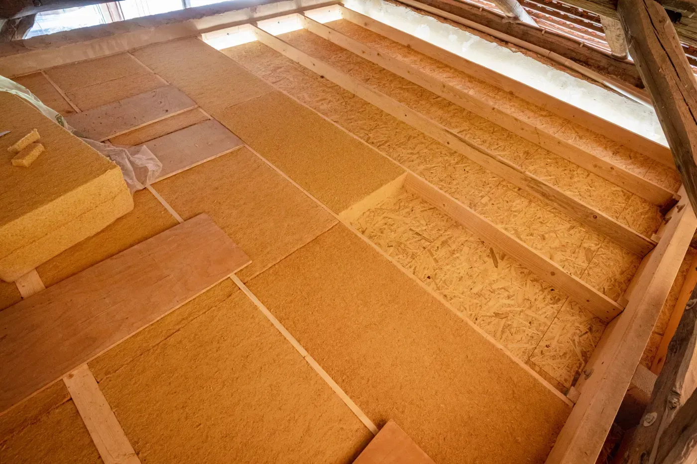 Holzboden im Dachgeschoss mit Dämmplatten und freiliegenden Balken unter warmem Licht