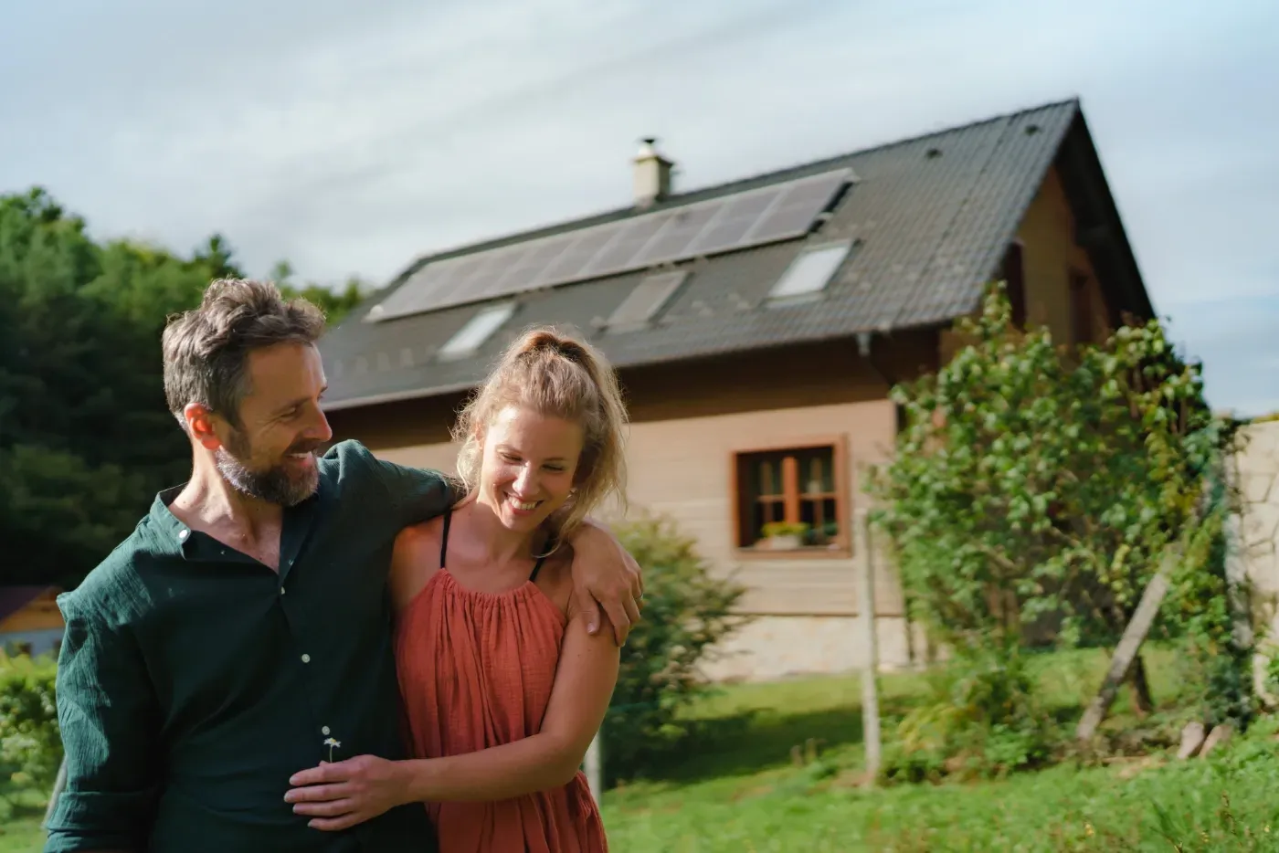 Ein Paar lächelt in einem Garten neben einem Haus mit Solarpaneelen auf dem Dach.