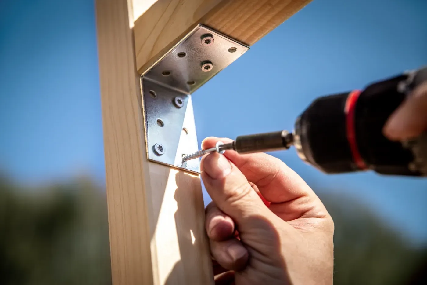 Eine Schraube von Hand in einen weißen Holzpfosten mit angebrachter Metallhalterung bohren.