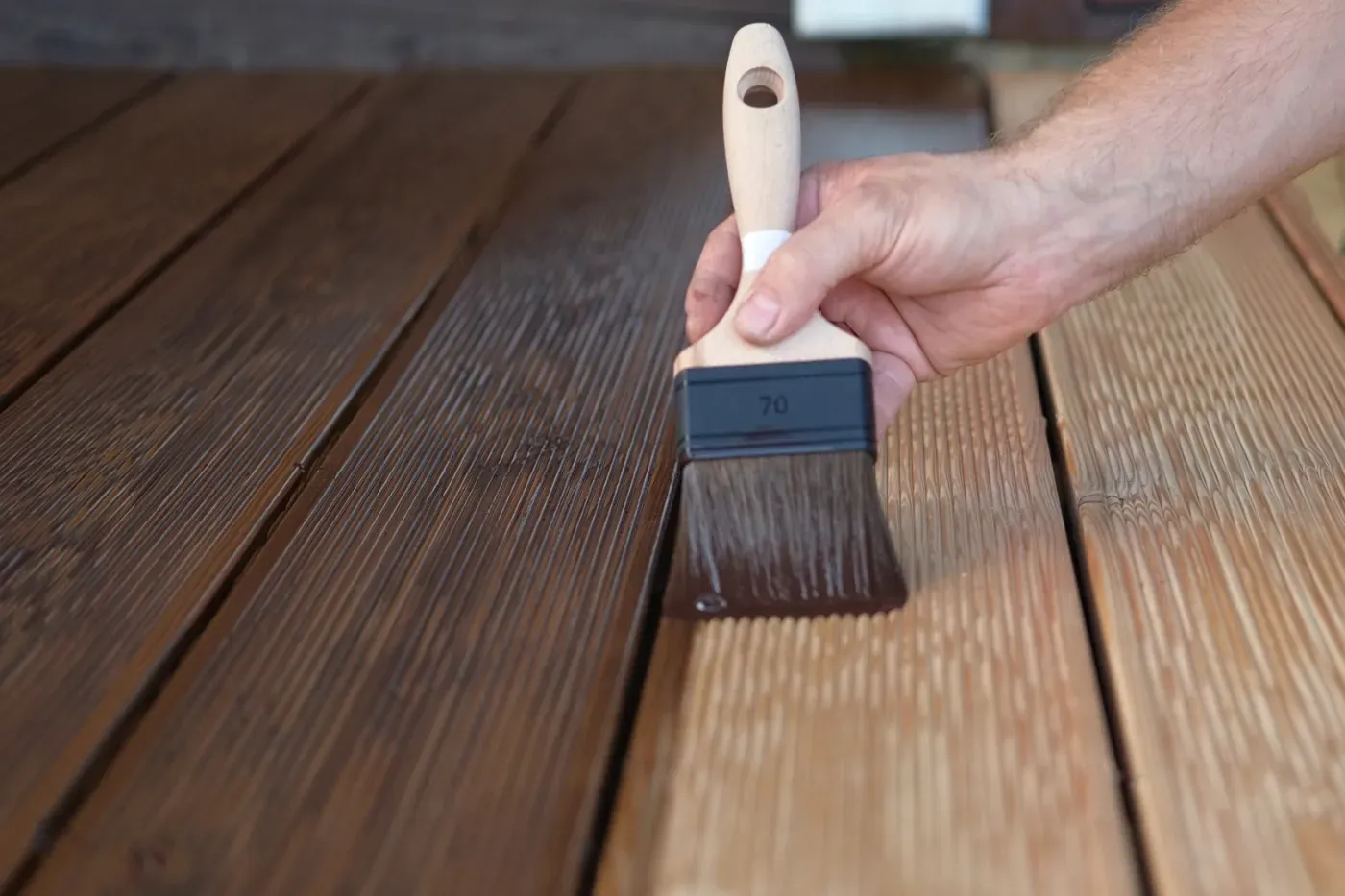 Eine Holzterrasse mit dem Pinsel von Hand streichen