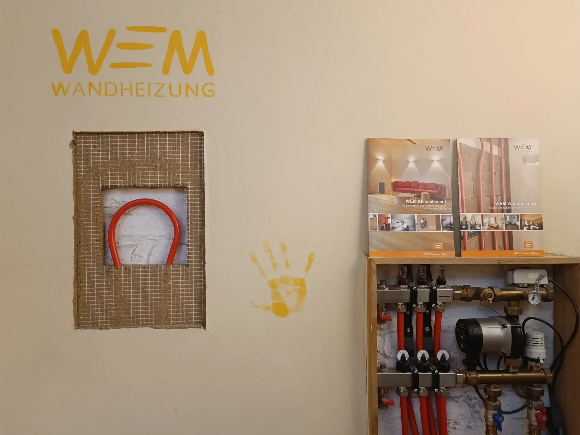 WAN HEIZUNG Wanddisplay mit Strahlungsheizpaneel und freiliegenden Sanitärinstallationen.