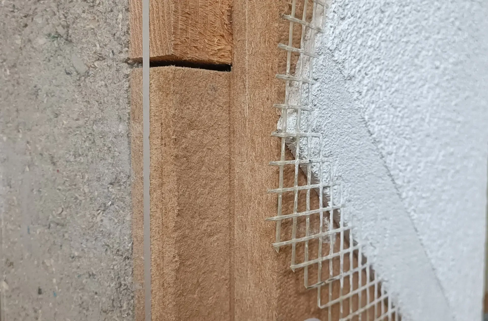 Nahaufnahme einer Wandecke mit rissigem Stuck, freiliegendem Drahtgeflecht und braunen Dämmplatten.