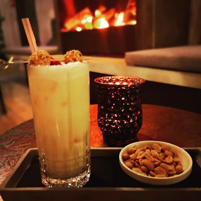 Hoher Cocktail, garniert mit Nüssen, brennender Kerze und Erdnüssen auf einem Tablett